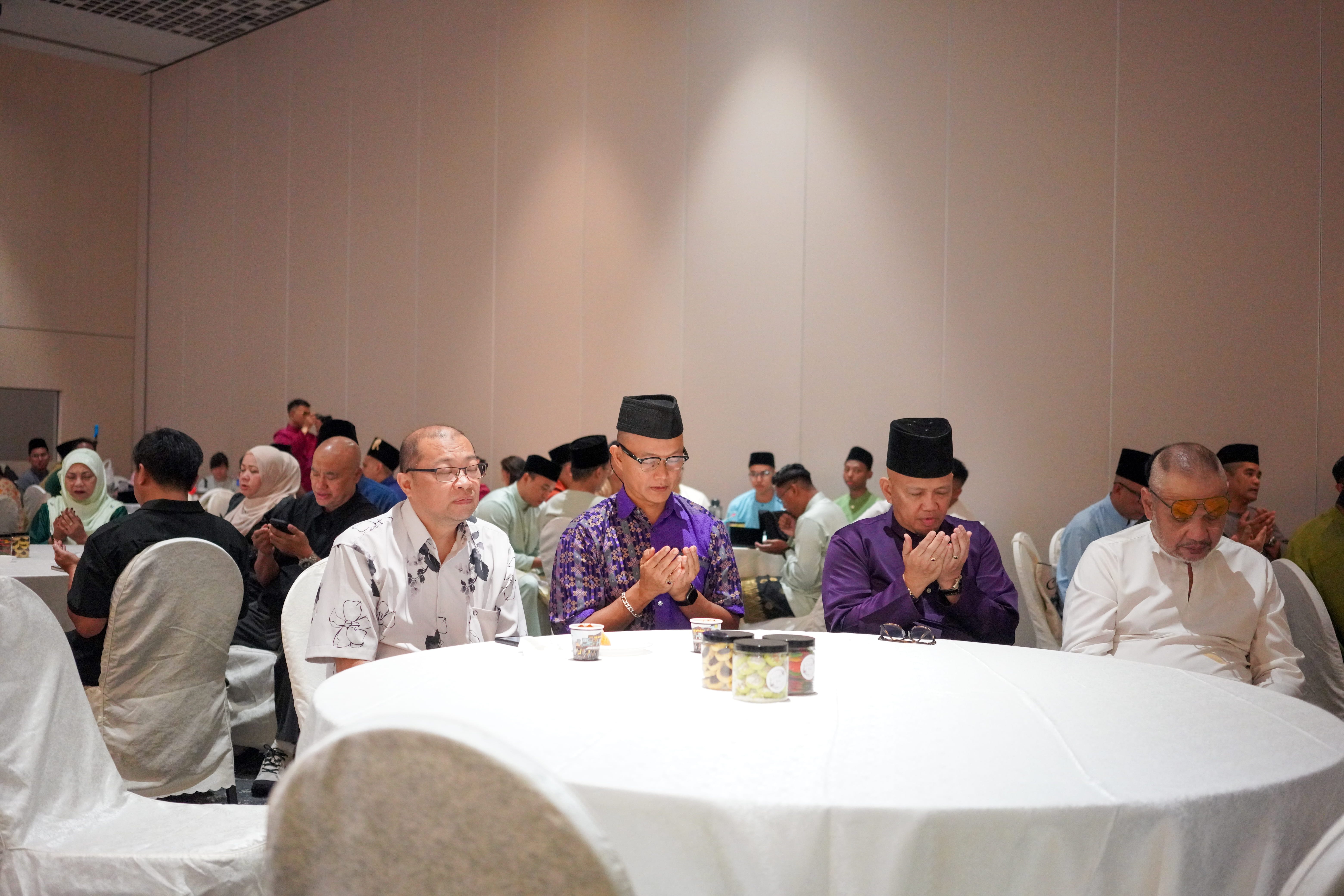Guests seated at a table participating in the opening prayer during the Annual General Meeting.
